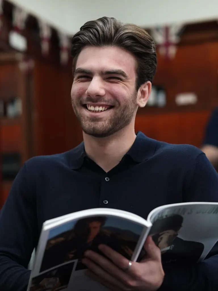 A customer laughing over a magazine in the chair at Pall Mall Barbers, shot by BarberOne