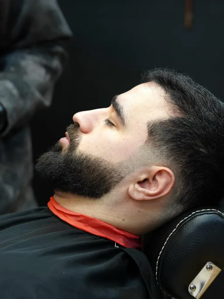 A customer reclined in the chair at AB Barbers in Putney while his beard is shaped